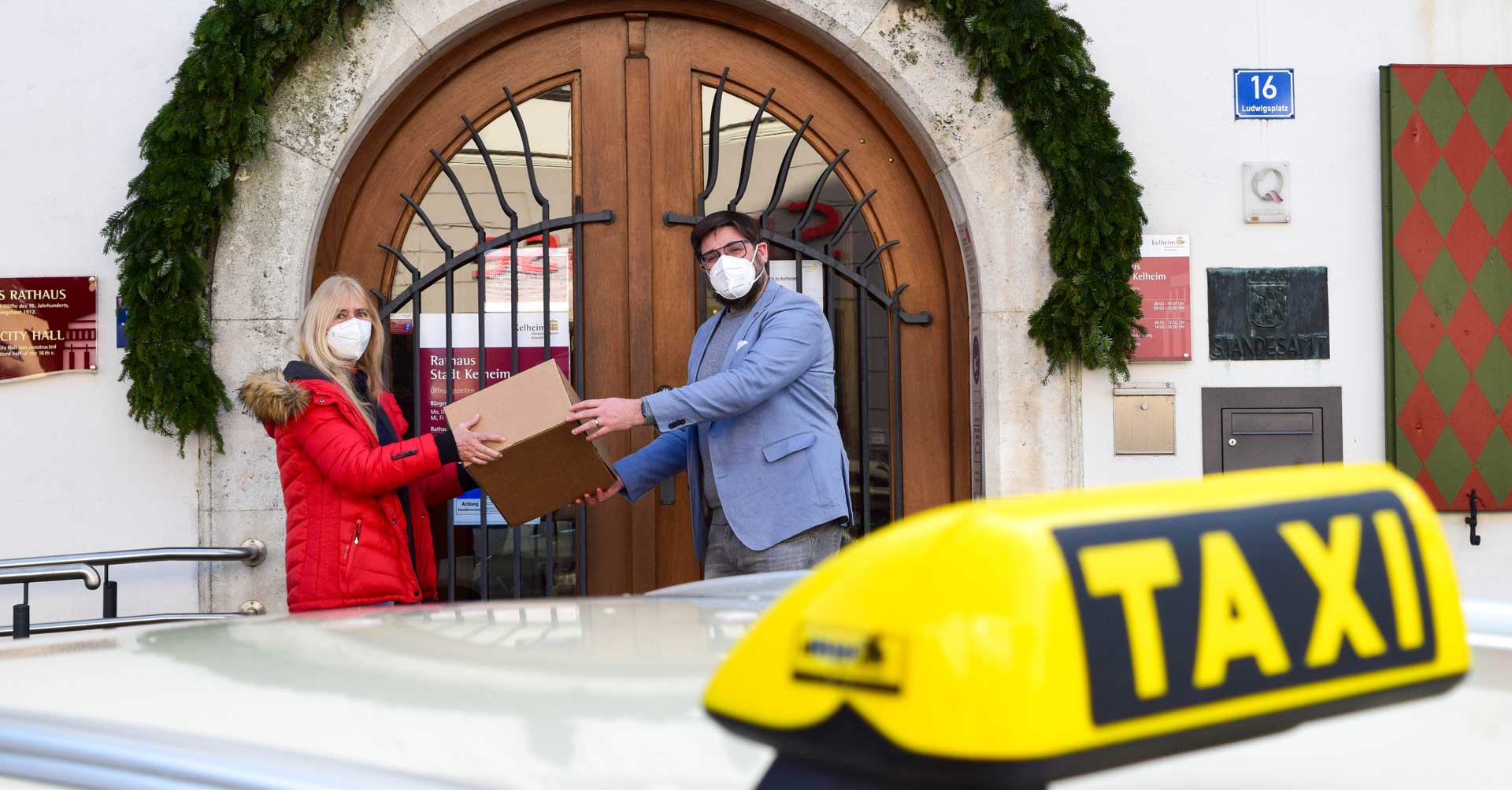 Persönlich bestellt, das Taxi liefert’s. Marion Hönig von MH-Taxi überreicht Bürgermeister Christian Schweiger vor dem Rathaus ein Paket (Foto: Lena Plapperer/Stadt Kelheim)