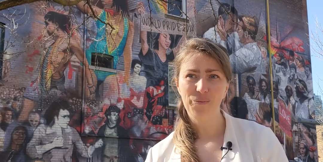 Freigeist-Fellow Tatiana Klepikova vor dem Mural „LGBTQ History and Community” von Christiano De Araujo am 519 Community Center in Toronto, Kanada. Screenshot aus dem Projektüberblick auf YouTube (in English) see https://youtu.be/vR1MlWmjjPU  (Foto: © Tatiana Klepikova)